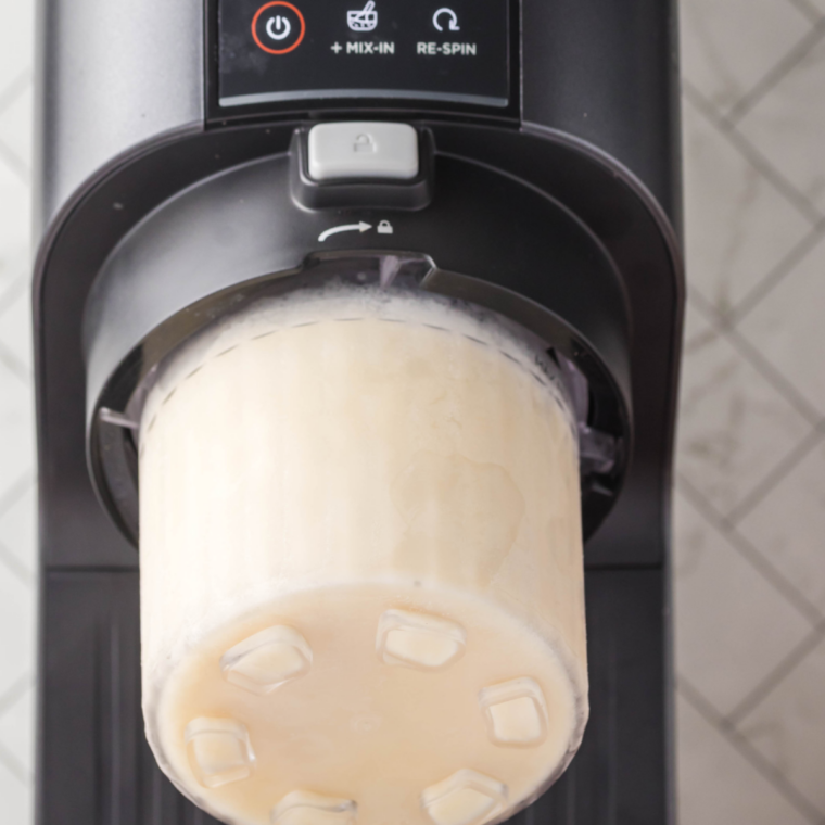 Frozen Ninja Creami pint locked into the outer bowl, running the Ice Cream function on the sweet cream base  