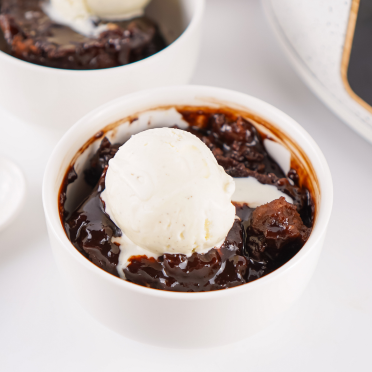 Warm crock pot chocolate cobbler in a white bowl with vanilla ice cream melting into the fudge sauce