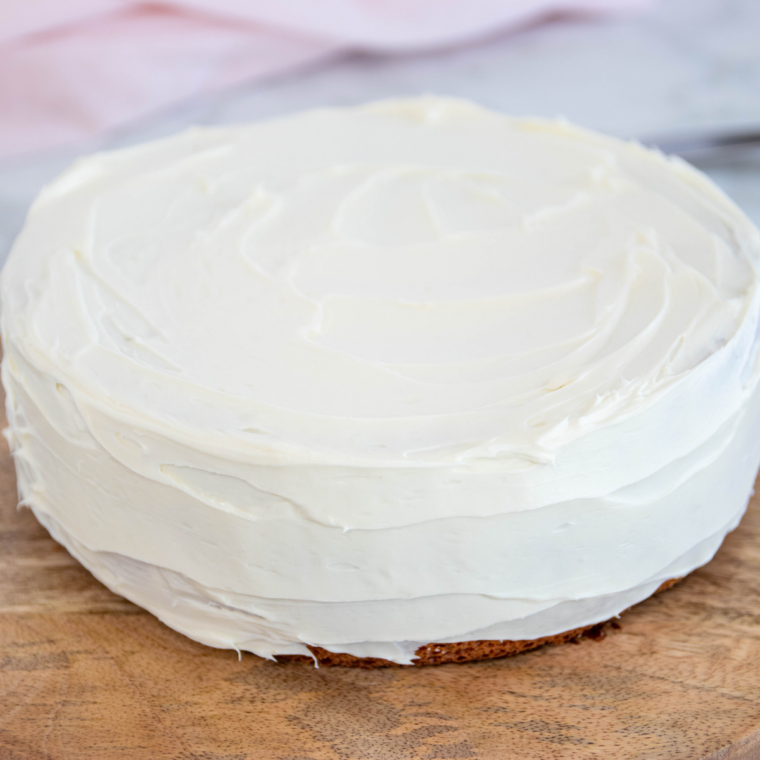 Whole white-frosted cake covered in rainbow sprinkles on a cutting board