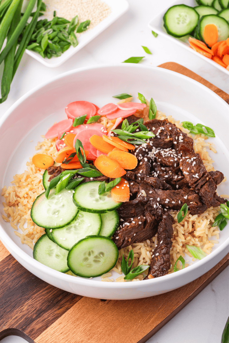 Two bowls, styled: Two Korean beef bulgogi bowls on a wooden table with chopsticks and kimchi