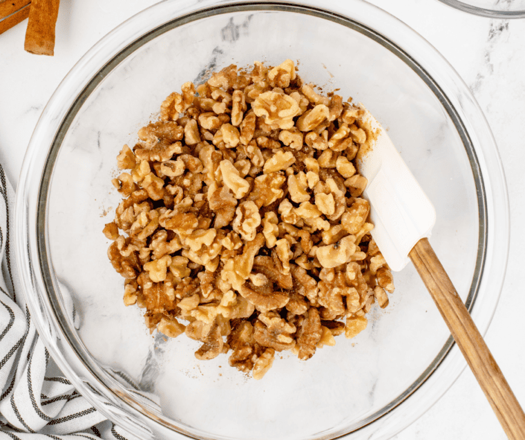 Walnuts tossed with sugar, instant coffee, cinnamon, and salt in a glass mixing bowl