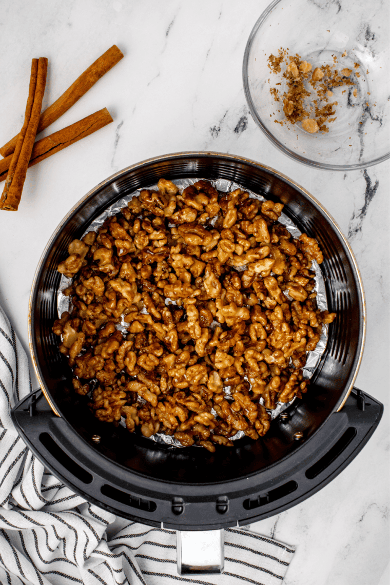 Coated walnuts spread in an even layer in a foil-lined air fryer basket