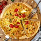 Air fryer egg tortilla frittata on a wooden cutting board with a fork, sliced into wedges