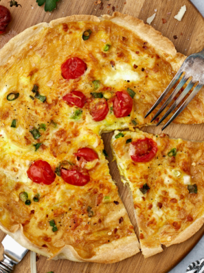 Air fryer egg tortilla frittata on a wooden cutting board with a fork, sliced into wedges