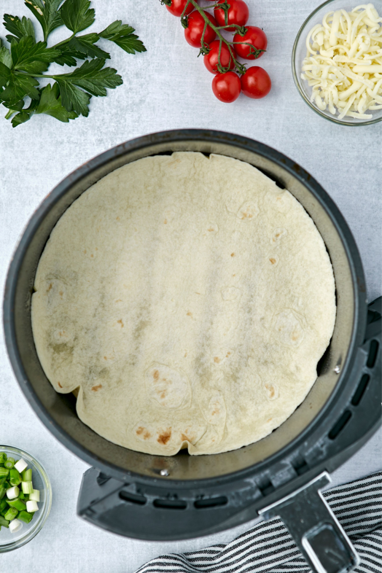 Flour tortilla pressed into a greased air fryer basket, edges ruffled and folded up the sides