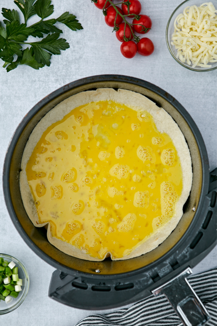 Egg mixture poured into a crisped tortilla shell in the air fryer basket