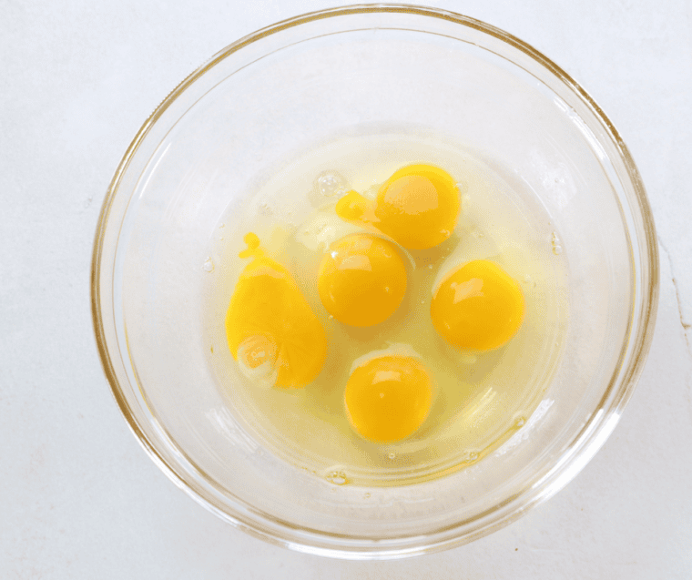 Eggs being cracked into a large glass mixing bowl
