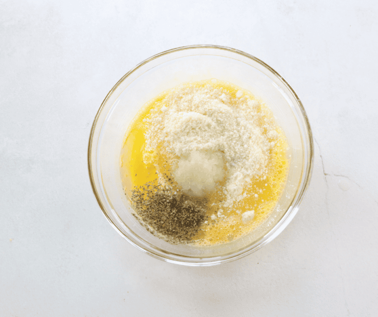 Eggs, oil, Parmesan, and seasonings whisked together in a large glass mixing bowl