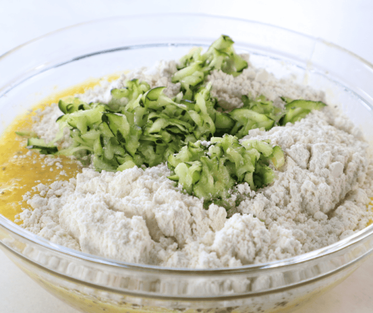 Grated zucchini being folded into the Bisquick and Parmesan batter with a spatula