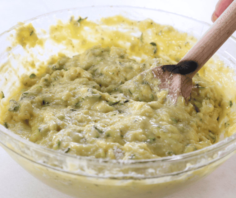 Shredded zucchini stirred into zucchini square batter in a large mixing bowl