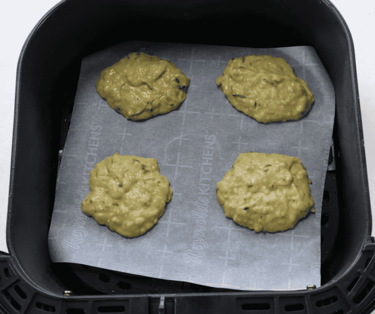 Cookie scoop dropping portions of zucchini batter onto parchment paper in an air fryer basket