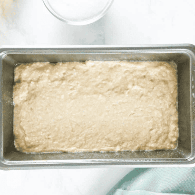 Banana bread batter in a parchment-lined loaf pan topped with walnuts before baking