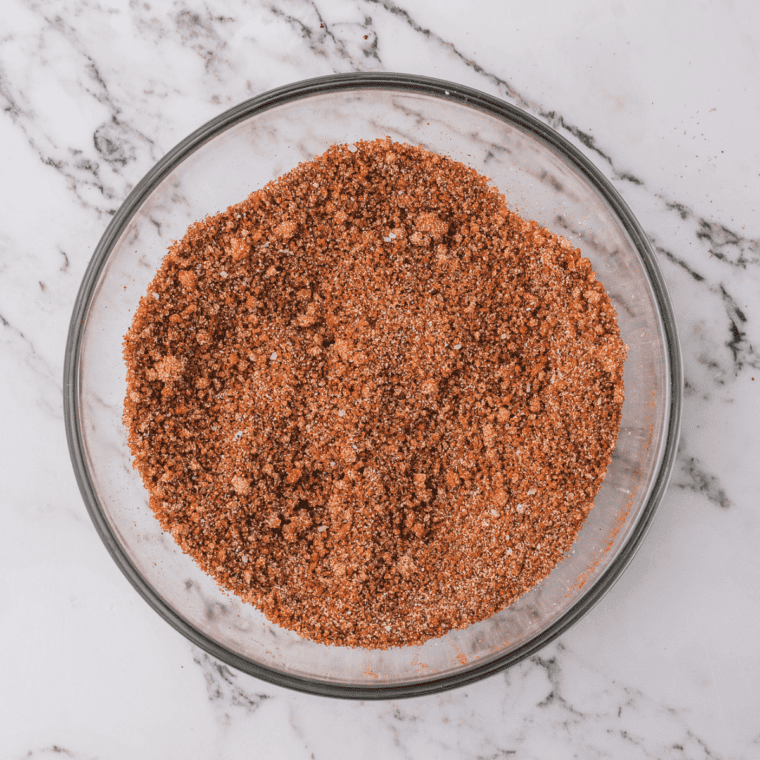 Mixed Bob Evans sausage seasoning blend in a small white bowl, flecked green with rubbed sage and red pepper