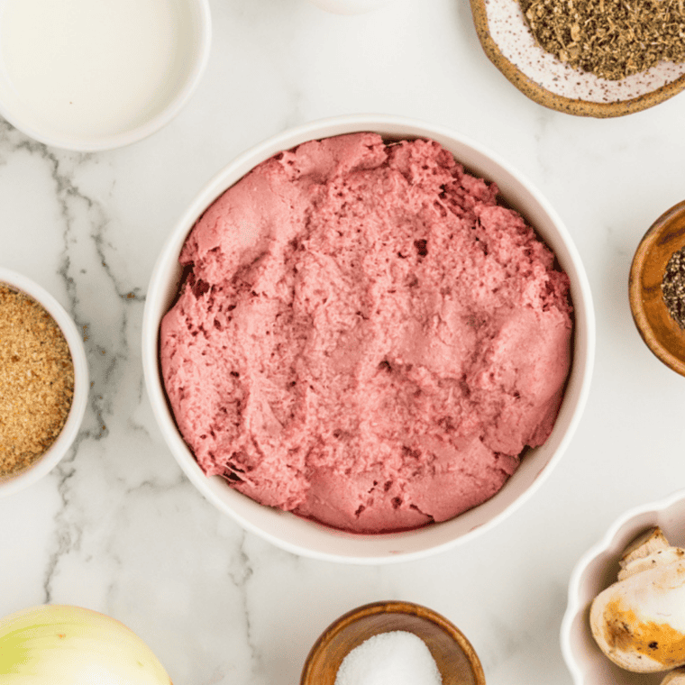 Overhead view of ground pork, sausage seasoning, and ice water arranged on a marble board