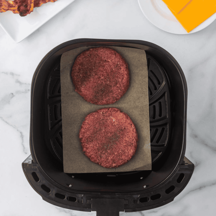 Eight raw breakfast sausage patties on a parchment-lined tray, each with a thumb dimple pressed into the center