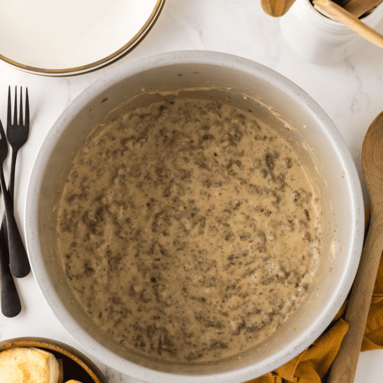 Sausage gravy simmering and thickening in a cast iron pan, stirred with a wooden spoon