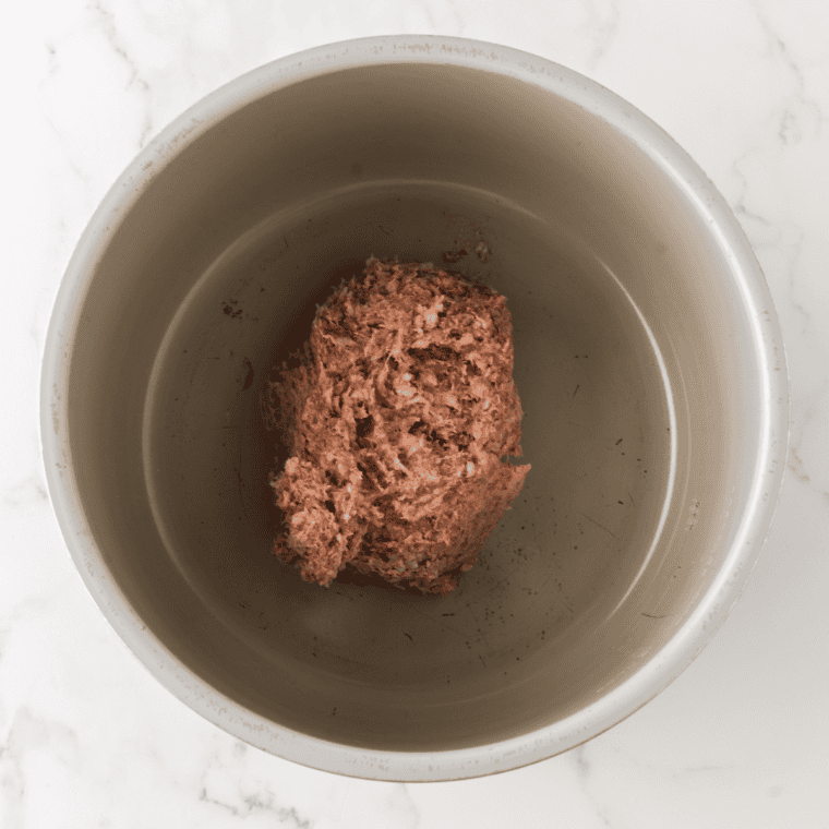 Ground pork sausage browning in a cast iron skillet, broken into nickel-sized pieces with a wooden spoon
