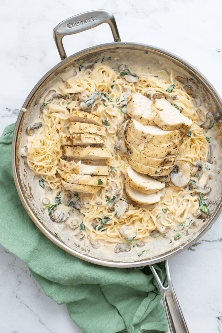 Pasta tossed with sliced chicken and mushroom cream sauce in a skillet