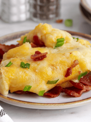 Chili's loaded mashed potatoes copycat in a white baking dish topped with melted cheddar jack cheese, crumbled bacon, and sliced chives