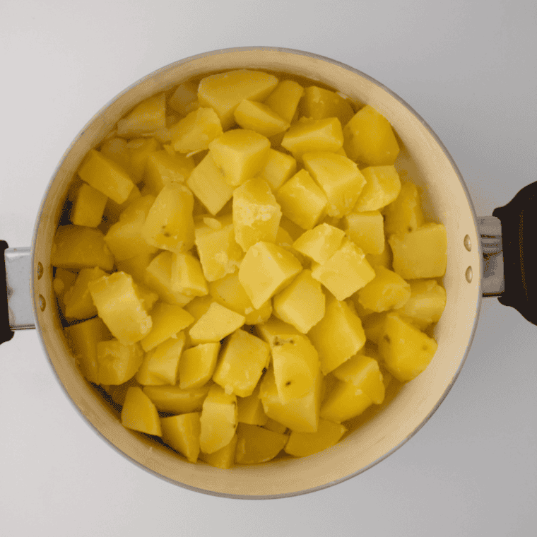 Potato chunks simmering in a pot, tested for doneness with a knife