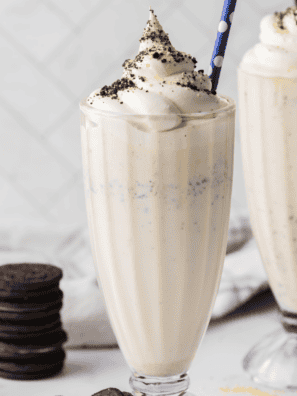 Copycat Chick-fil-A cookies and cream shake in a tall glass topped with whipped cream, crushed Oreo pieces, and a maraschino cherry
