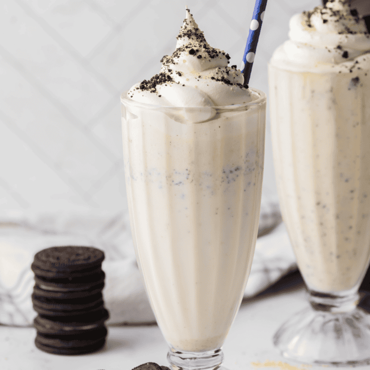 Copycat Chick-fil-A cookies and cream shake in a tall glass topped with whipped cream, crushed Oreo pieces, and a maraschino cherry