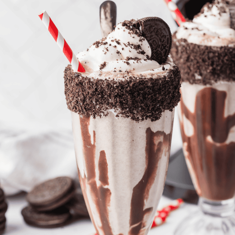 Copycat Chick-fil-A cookies and cream shake in a tall glass topped with whipped cream, crushed Oreo pieces, and a maraschino cherry