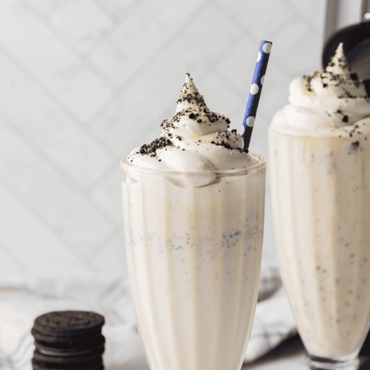 Copycat Chick-fil-A cookies and cream shake in a tall glass topped with whipped cream, crushed Oreo pieces, and a maraschino cherry