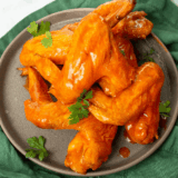 Crispy chicken wings coated in homemade copycat Frank's RedHot sauce on a gray plate