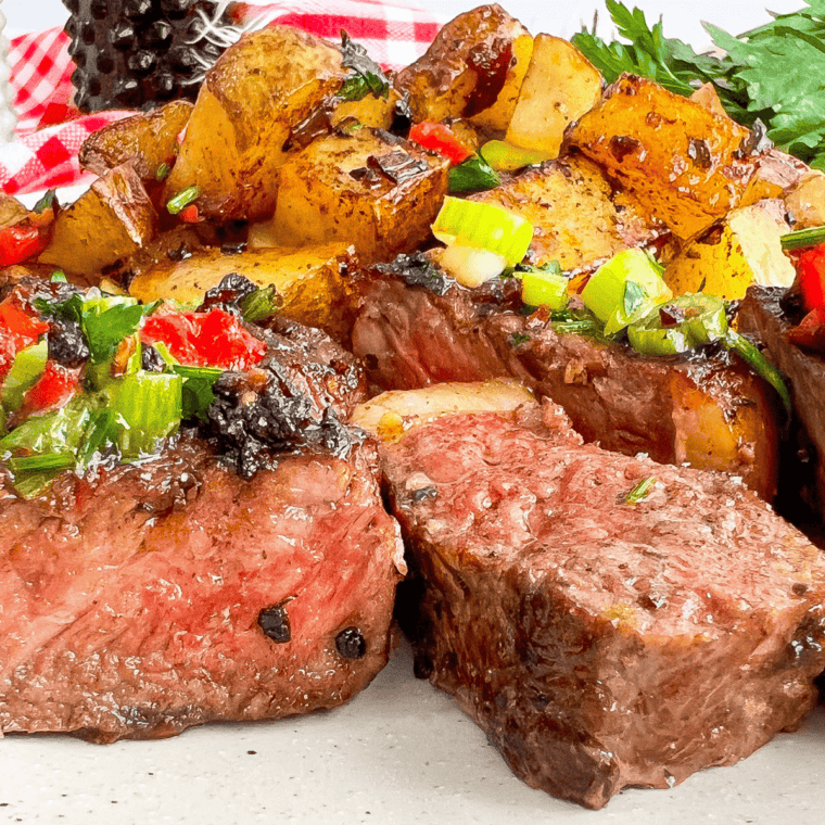 Sliced steak on a white plate topped with copycat Kinder's Buttery Garlic and Herb seasoning and melting butter