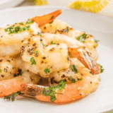 Lemon pepper shrimp arranged on a white plate with lemon wedges