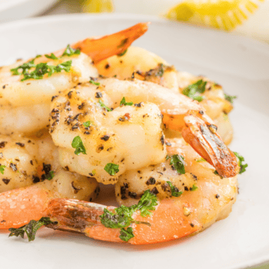 Lemon pepper shrimp arranged on a white plate with lemon wedges