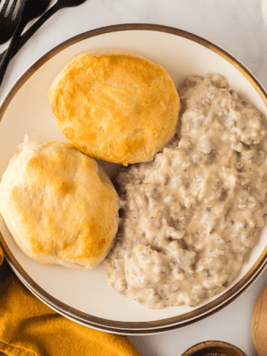 Homemade sausage gravy ladled over split biscuits with visible black pepper