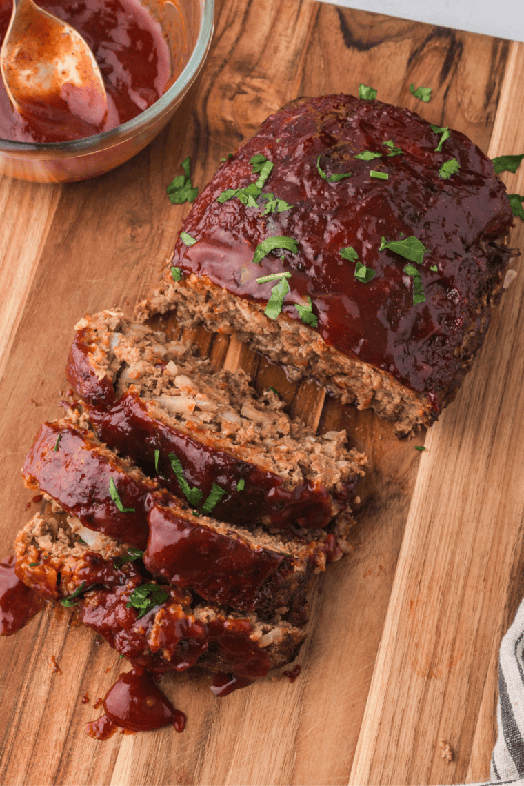 Copycat McCormick meatloaf sliced on a cutting board with a jar of homemade seasoning mix