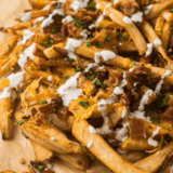 Copycat Outback Aussie cheese fries on a sheet pan topped with melted Monterey Jack, cheddar, and crispy bacon with spicy ranch on the side