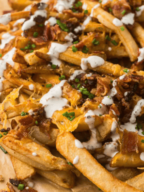 Copycat Outback Aussie cheese fries on a sheet pan topped with melted Monterey Jack, cheddar, and crispy bacon with spicy ranch on the side