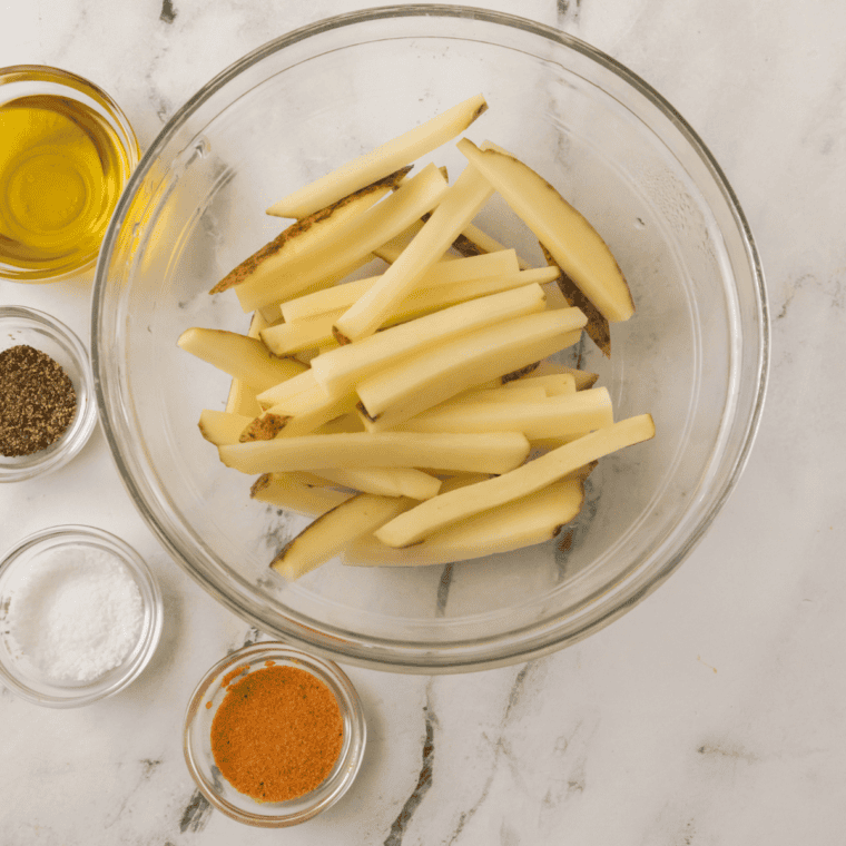 Skin-on russet potatoes cut into half-inch sticks soaking in a bowl of cold water for Aussie cheese fries