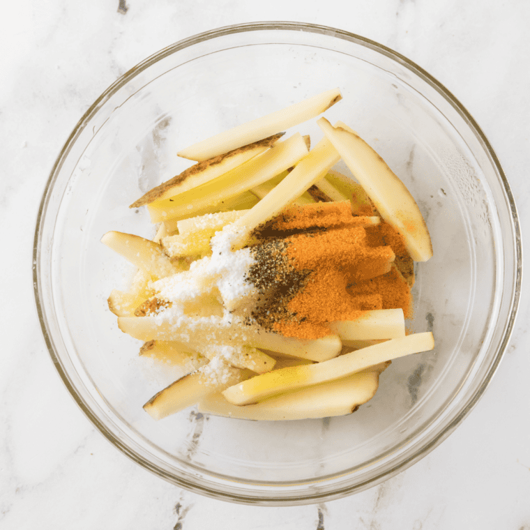 Potato fries tossed with cornstarch, oil, and Aussie fries seasoning blend of paprika, garlic powder, and cayenne in a large bowl