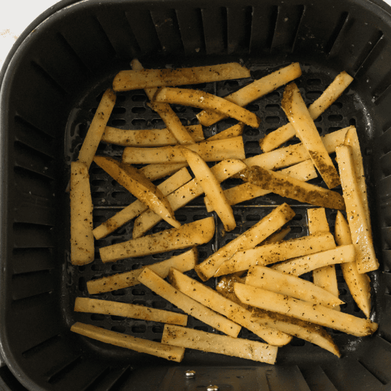 Seasoned fries in a single layer in an air fryer basket cooking at 400 degrees until deeply golden