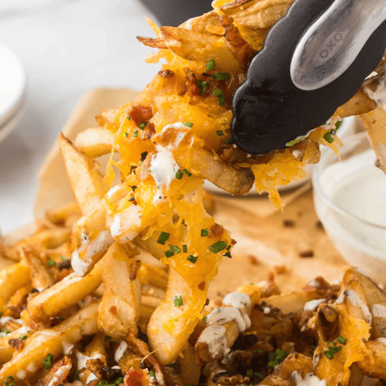 Copycat Outback Aussie cheese fries loaded with melted Monterey Jack, cheddar, and crispy bacon with spicy ranch alongside