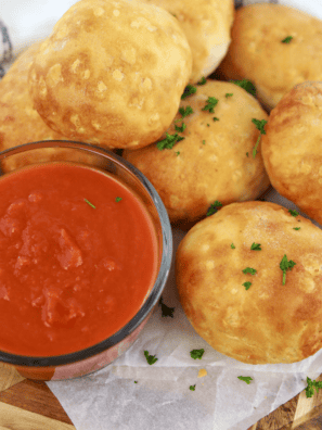 Copycat Pizza Hut pizza sauce in a small bowl with pizza rolls on a wooden table
