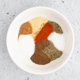 Bowl of copycat Ruth's Chris steak seasoning beside a raw ribeye coated in the spice blend