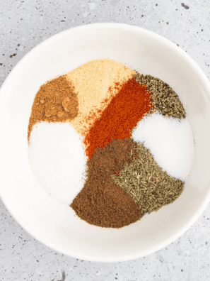 Bowl of copycat Ruth's Chris steak seasoning beside a raw ribeye coated in the spice blend