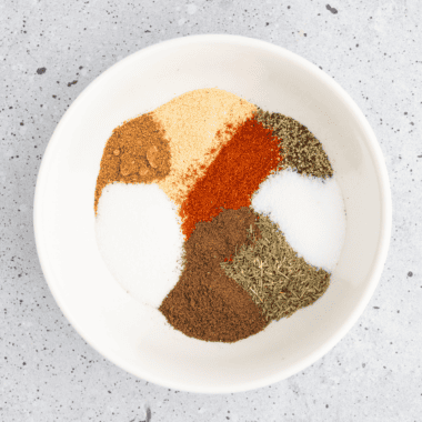 Bowl of copycat Ruth's Chris steak seasoning beside a raw ribeye coated in the spice blend