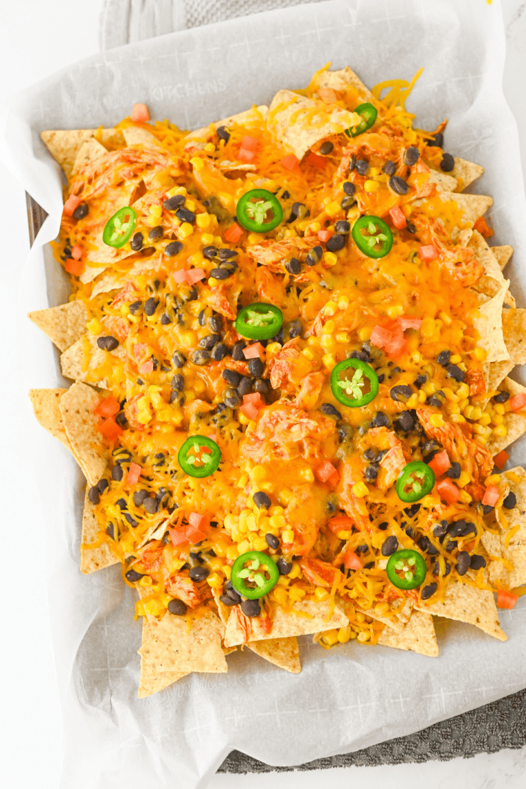 Finished crockpot chicken nachos topped with chopped Roma tomatoes and sliced jalapeños