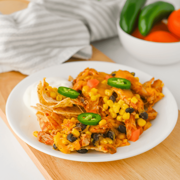 Plate of crockpot chicken nachos with shredded chicken, melted cheddar, black beans, corn, tomatoes, and jalapeños