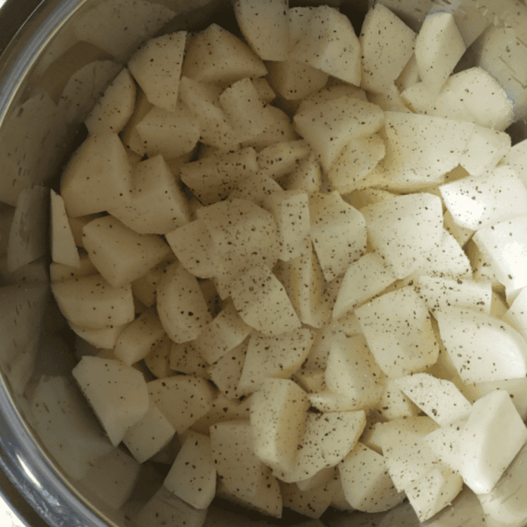Parboiled potato cubes draining in a colander with steam rising