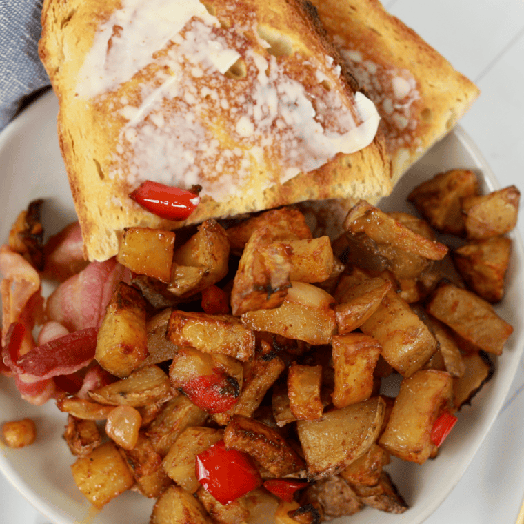 Denny's home fries served on a white plate with two fried eggs and bacon  