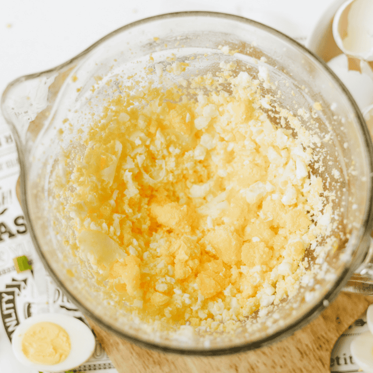 Baked eggs being blended into fine crumbles with a hand mixer in a glass mixing bowl