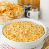 Bowl of football dip on a game day snack table with chips, wings and cold drinks